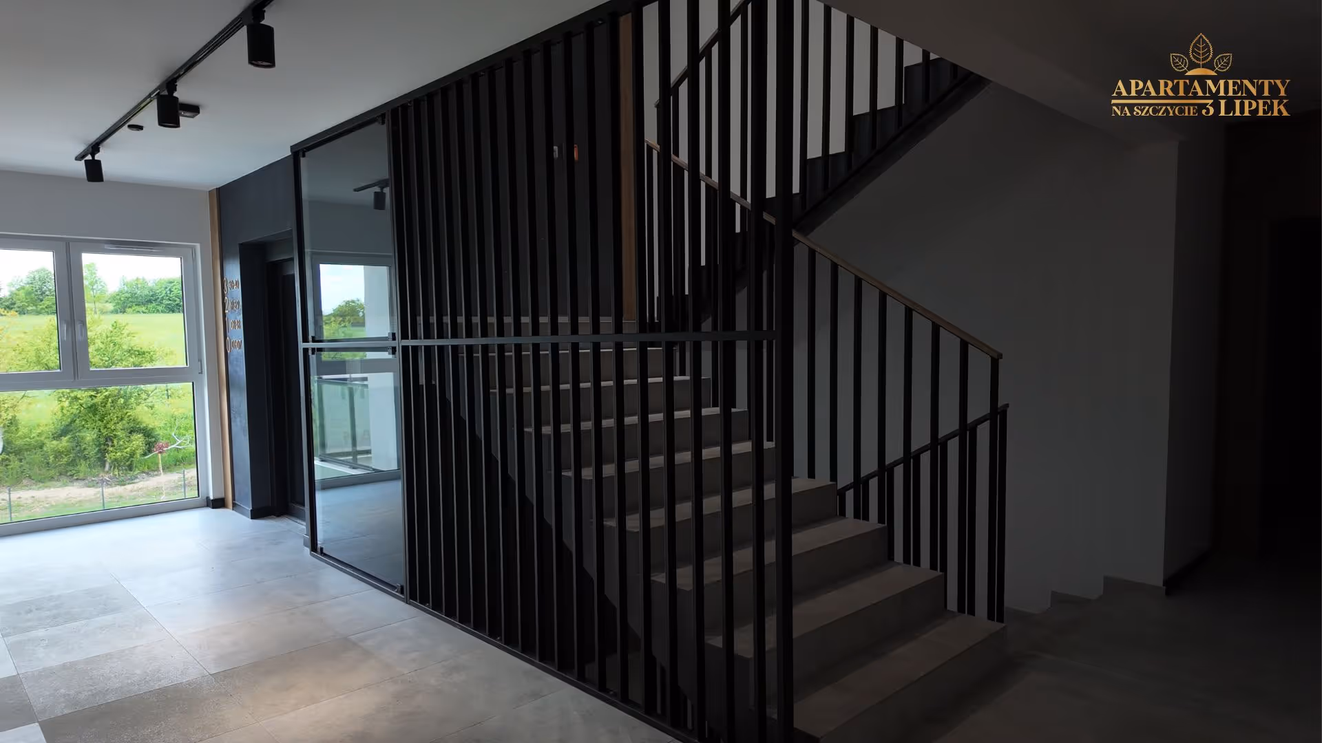 Przestronne wnętrze klatki schodowej z czarną balustradą, betonowymi schodami i dużym oknem.